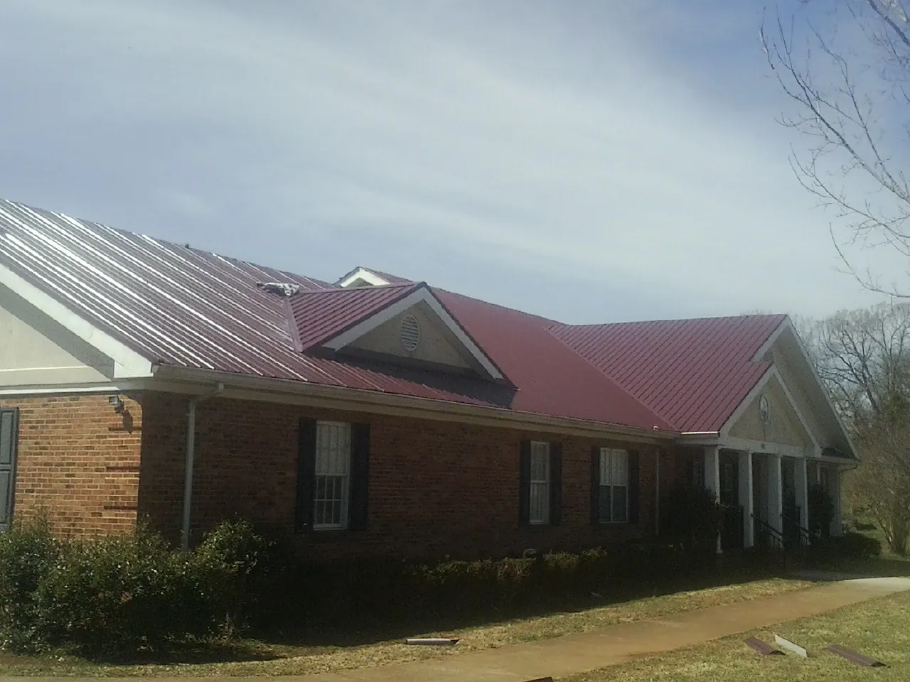 Red metal roof with gabled entries on a long brick building, from a Hail Damage Roof Repair job in Longmeadow