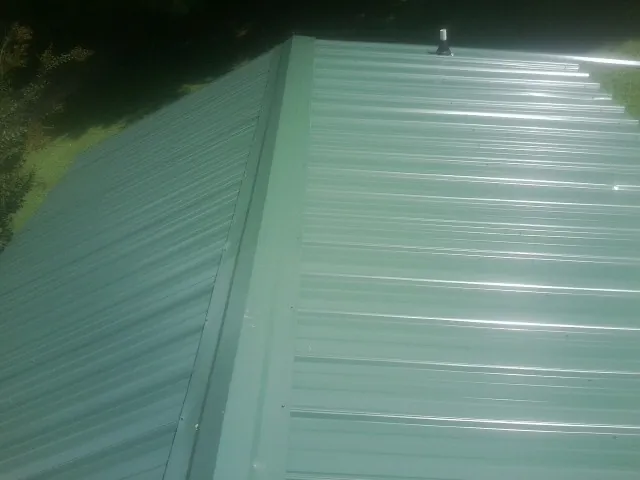New green metal panels meeting at the ridge of a roof — Flat Roof Repair work by our crew in Longmeadow