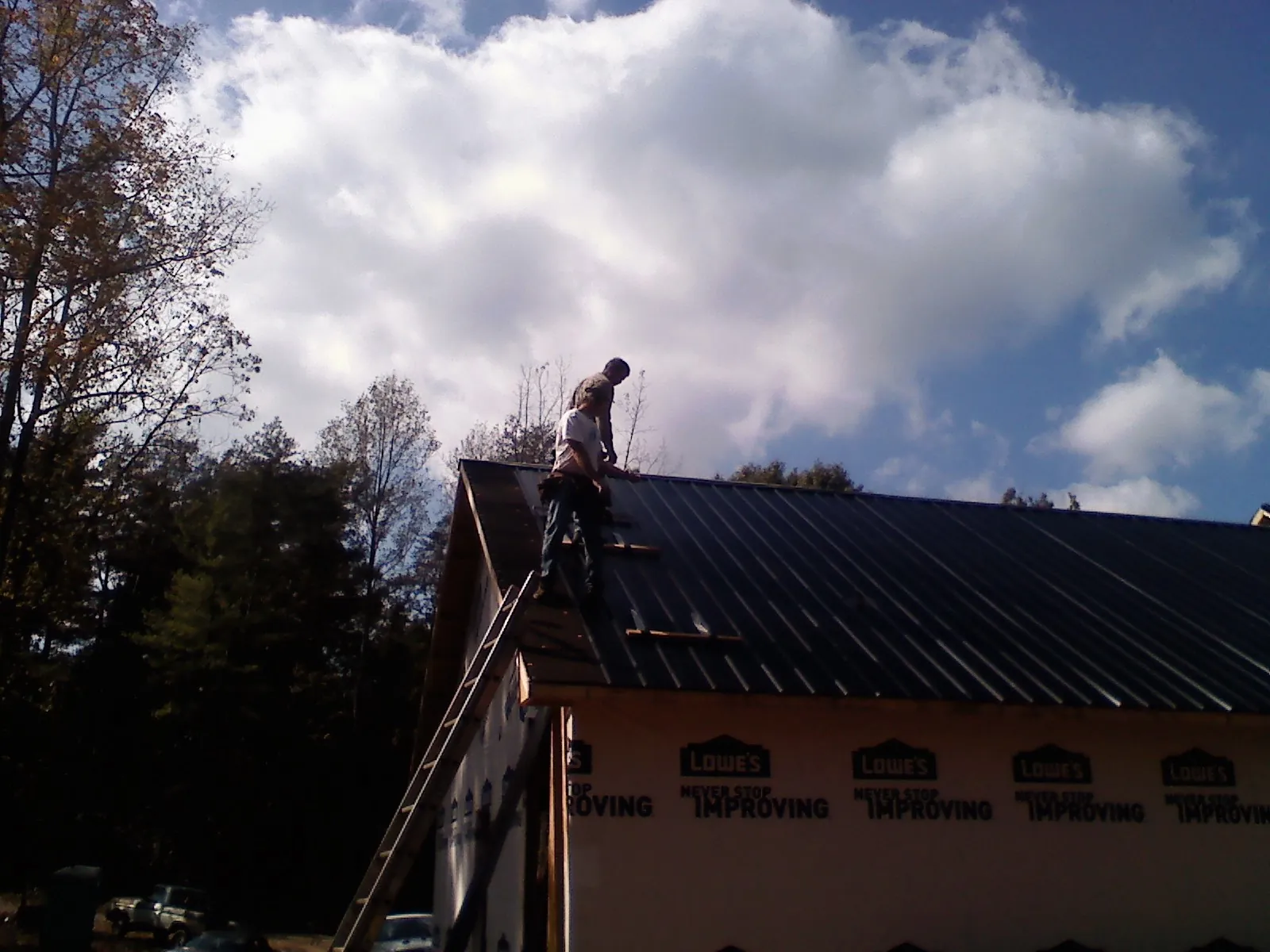 Roofer fastening dark metal panels high against a cloudy sky, from a Roof Inspection job in Longmeadow